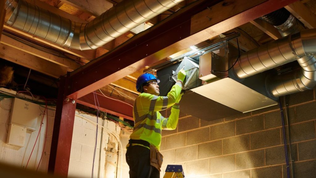 A man is on a ladder trying to remove a ducted aircon filter in order to clean it