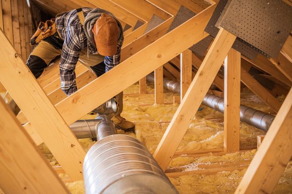 An HVAC technician installing ducts in the wooden attic space