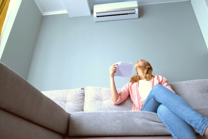 Woman Looking at Broken Air Conditioner Sitting on Couch