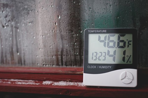 A hygrometer for humidity control showing high values in a window corner